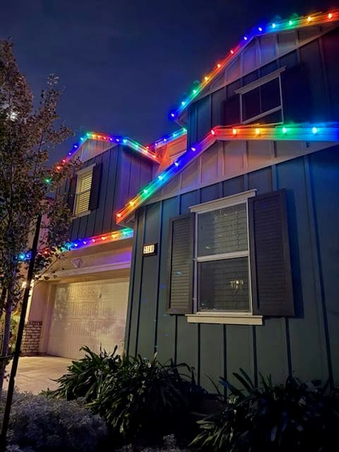 Colorful holiday lights adorn a home's roof and eaves at night, enhancing its festive charm.