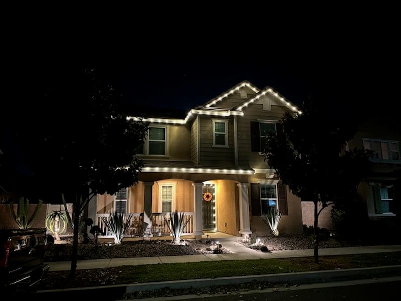 Cozy home illuminated at night with festive lights and desert plants in the yard.